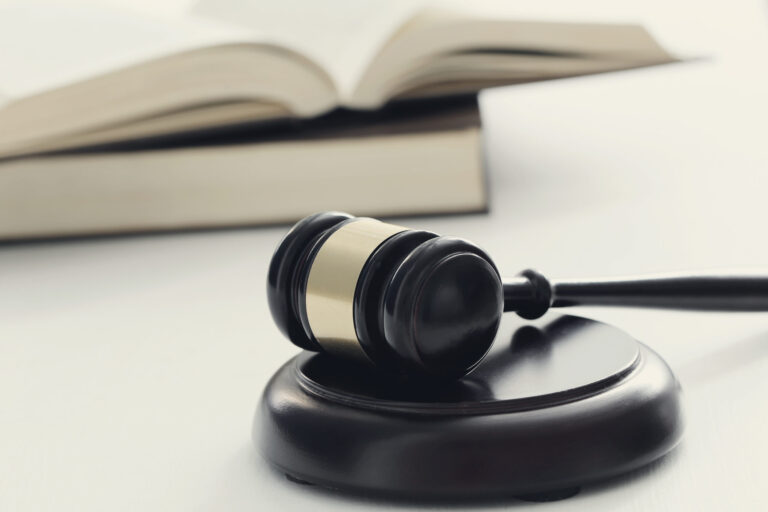 A wooden gavel rests on a sound block, symbolizing law and justice. In the background, an open book hints at 2024 compliance trends in employment law, offering a glimpse into the legal landscape. The image maintains a soft, neutral tone.
