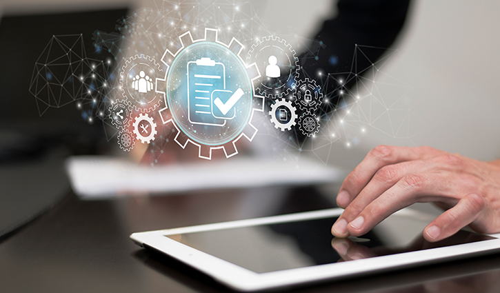 Close-up of hands using a tablet, overlaid with digital icons like gears and a clipboard with a checkmark, symbolizing workflow automation and project management. The blurred workspace in the background hints at preparing for Open Enrollment 2025 efficiently.