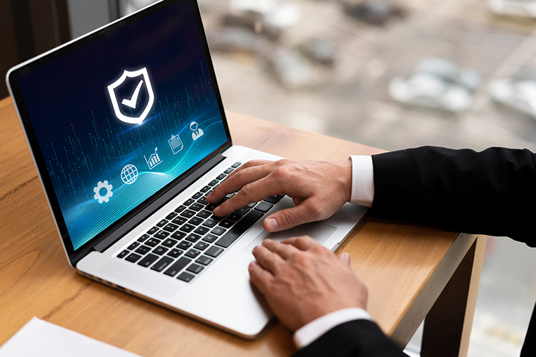 A person in a suit uses a laptop displaying a cybersecurity interface with a shield icon and network symbols, suggesting data protection and secure online activity in the modern market.