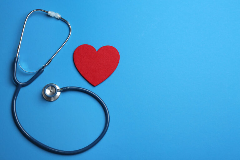 A stethoscope is arranged on a blue background with its tubing forming a loose loop. Beside it, a red heart cutout adds a pop of color, symbolizing health and care—an ideal image for illustrating comprehensive Health Plans.