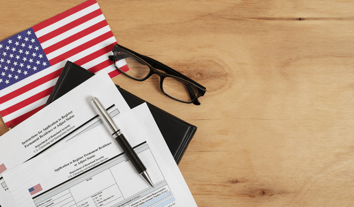 U.S. flag, eyeglasses, a pen, and paperwork titled Application for Permanent Residence rest on a wooden surface, hinting at the intricate process of immigration or legal documentation through USCIS.