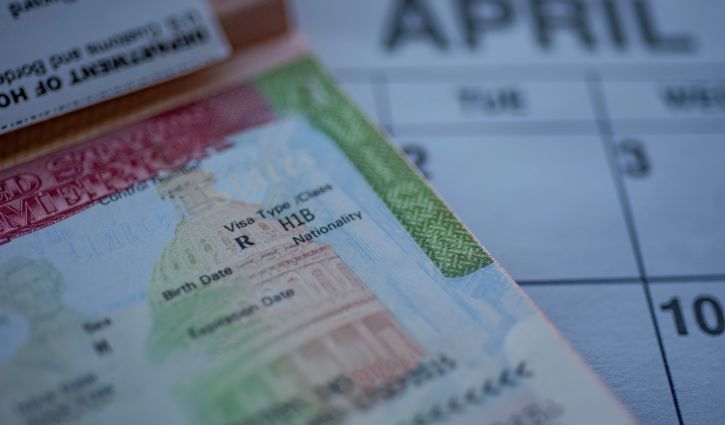 H1B visa (for specialty workers) stamp in passport, blurred april calendar on background. H1B visa program deadline concept. Close up view.