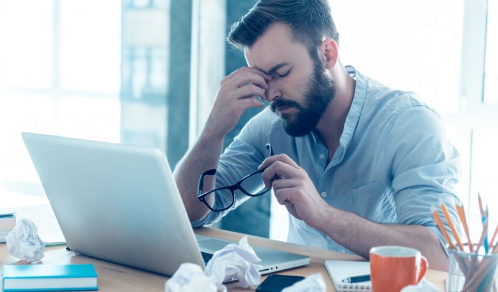 Feeling exhausted. Frustrated young beard man massaging his nose and keeping eyes closed while sitting at his working place in office