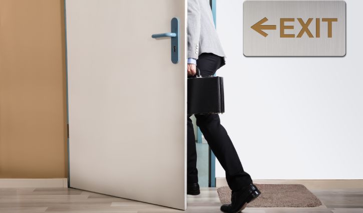 Businessperson Walking Out With Exit Sign On Wall