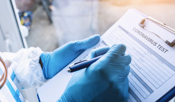 Doctor fills out a coronavirus test data sheet with pen in protective clothing in a clinic leaning against window at Covid-19 coronavirus epidemic