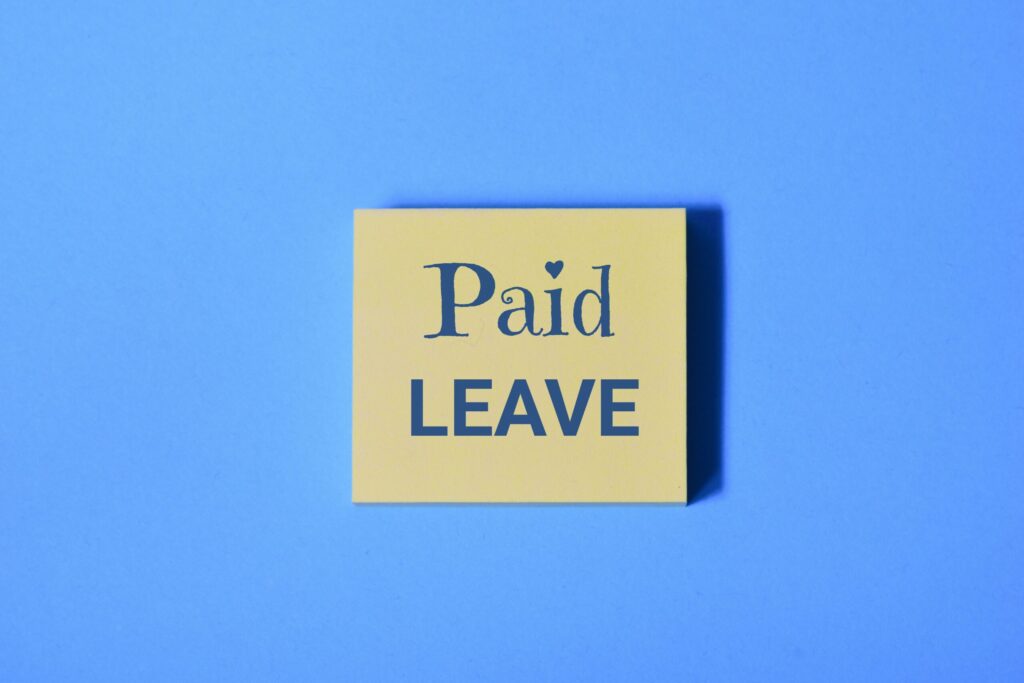 A yellow sticky note with the words Paid Leave in bold letters stands out against a blue background, symbolizing the expanding reach of Paid State Leave Laws.