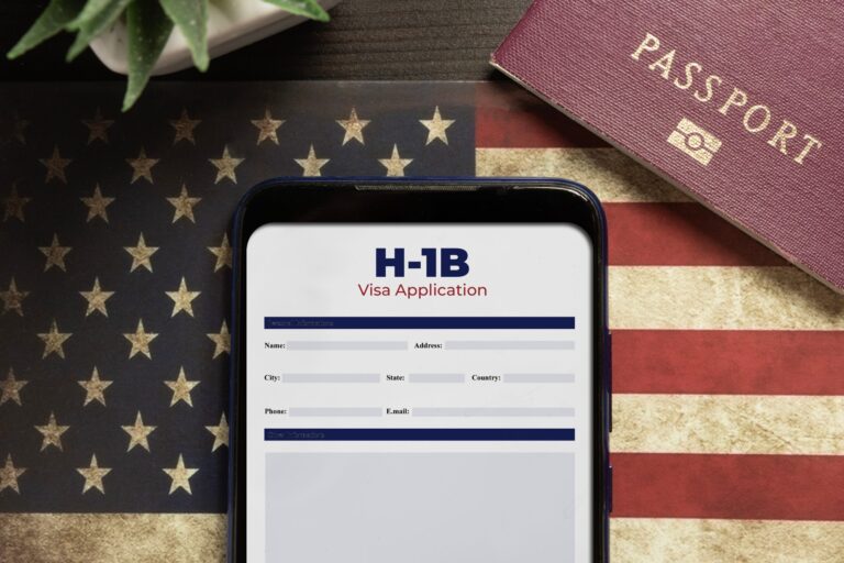A smartphone showing an H-1B visa renewal form is placed on a U.S. flag background. A passport and a corner of a green plant are visible, symbolizing the hope and continuation of ones journey in the domestic landscape.