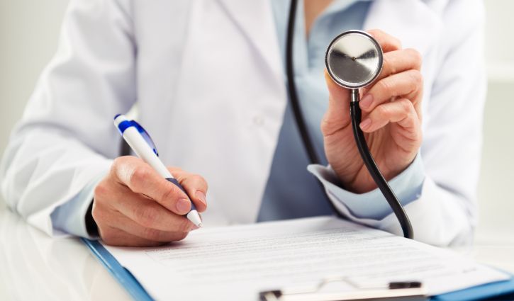 Closeup of doctor physician reporting medical test results. Woman medic in uniform filling health insurance document in the office. Shallow depth of field.