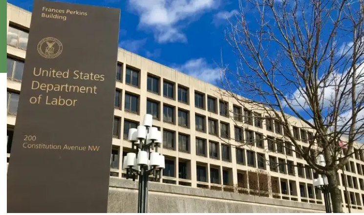 Sign for the United States Department of Labor at Frances Perkins Building, 200 Constitution Avenue NW. The modern building stands under a blue sky with clouds and a leafless tree to the right. Discussions on the Proposed Overtime Rule echo within its walls, capturing attention far beyond TechServe Alliance circles.