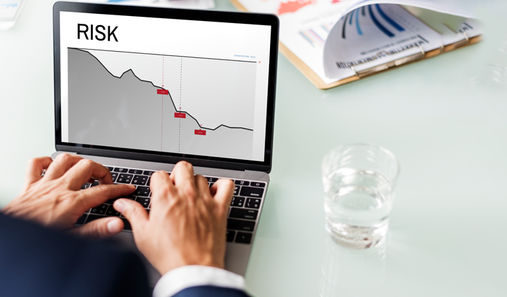 A person using a laptop displaying a graph labeled Risk Insights with a downward trend and marked points. A glass of water and documents with charts are on the desk, highlighting common sources of D&O liability.