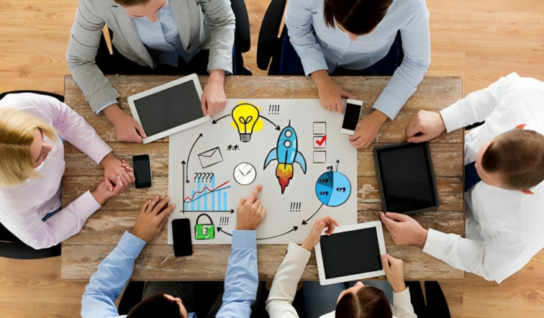 Around a table, people engage with tablets, discussing vibrant drawings: a rocket, light bulb, and graphs. This lively roundtable scene hints at a creative brainstorming or business strategy meeting among industry peers from TechServe Alliance.