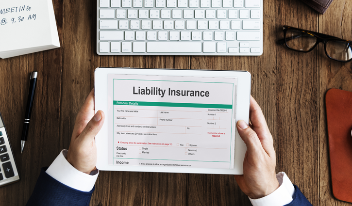 A person in a suit holds a tablet showing an Employment Practices Liability Insurance form. The table, adorned with a keyboard, glasses, and notepad, hints at a professional workspace where careful attention to such insurance matters is paramount.